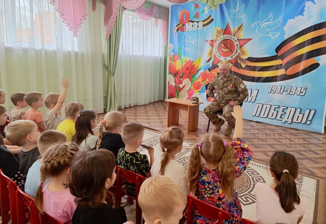 Сегодня в дошкольном отделении МБОУ СОШ №1 им. Героя Советского Союза И.И. Иванова (ул. Институтская, 2А) состоялась волнующая встреча с участником специальной военной операции, рядовым мотострелковых войск Павлом Викторовичем Костеневкиным. Павел Викторович рассказал ребятам о важном значении СВО, о любви к Родине и готовности защищать родных и близких. Он поделился историями о мужестве и героизме своих сослуживцев, рассказал, какими качествами должен обладать современный солдат и как важно преодолевать трудности войны. Настоящий герой нашего времени подчеркнул, что поддержка и вера в победу родных и всей страны помогают справиться со всеми трудностями на передовой и поддерживают боевой дух. Урок мужества прошел в теплой и дружеской обстановке. Ребята увидели на конкретном примере, что герои живут рядом, и что мужество, храбрость и любовь к Родине – это качества настоящего патриота и гражданина России. В завершение мероприятия дошкольники прочитали стихи о Родине и Дне Победы, передали на фронт открытки и письма, сделанные своими руками для наших бойцов.